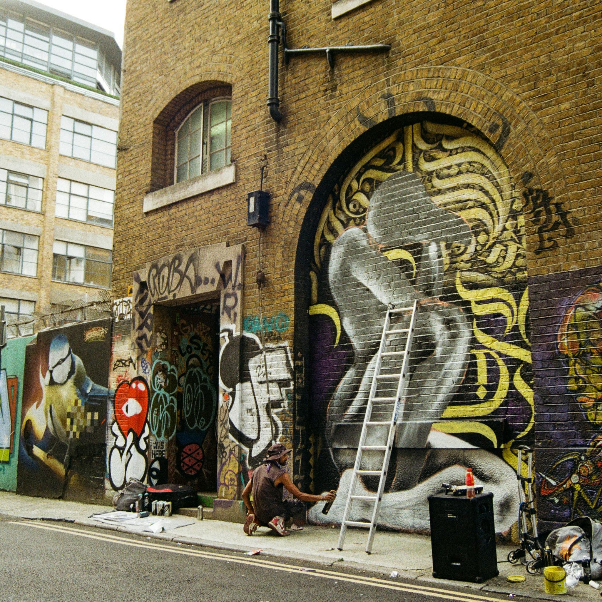 Graffiti art on a brick wall with a person painting, in an urban setting.