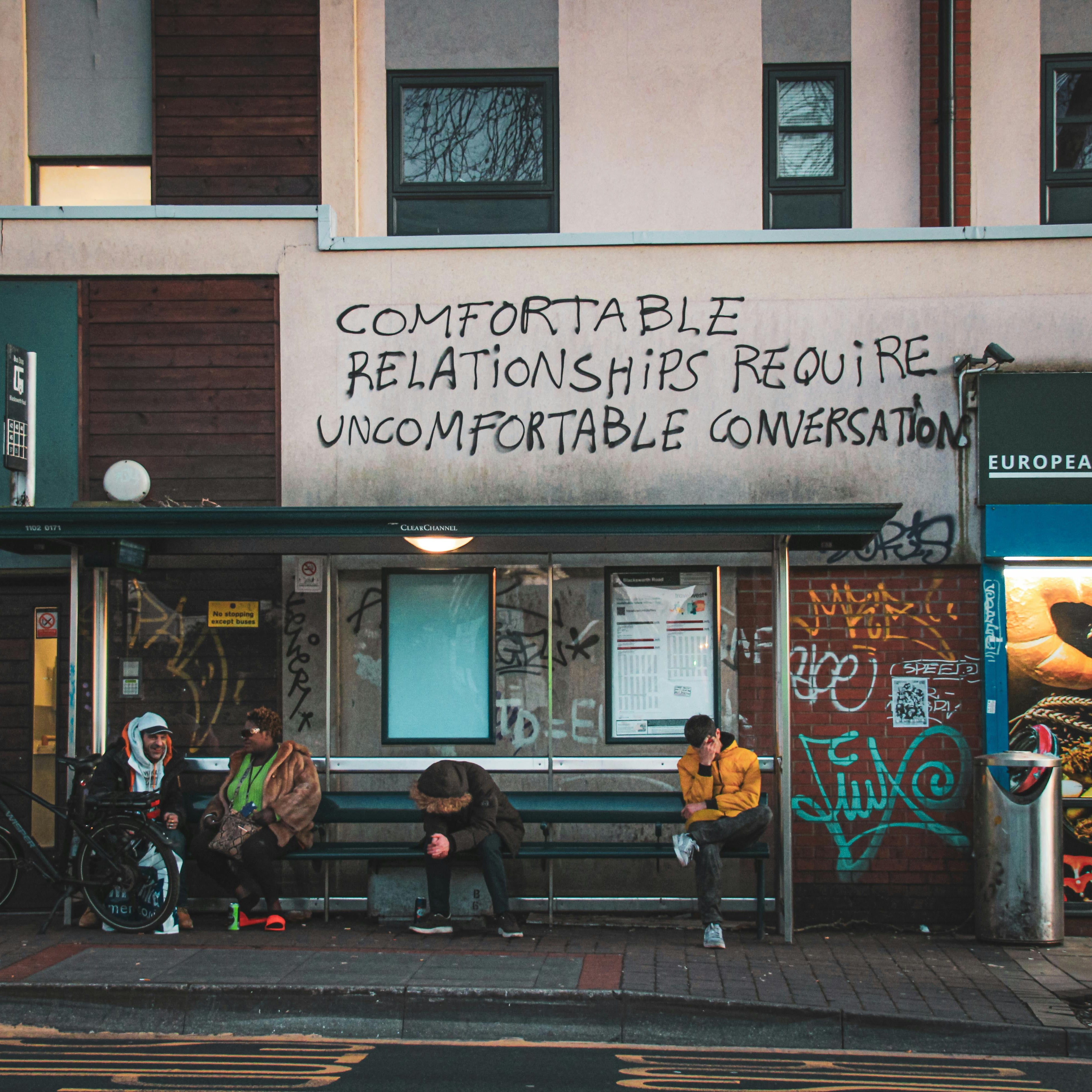 People sitting on a bench with graffiti on a building wall.